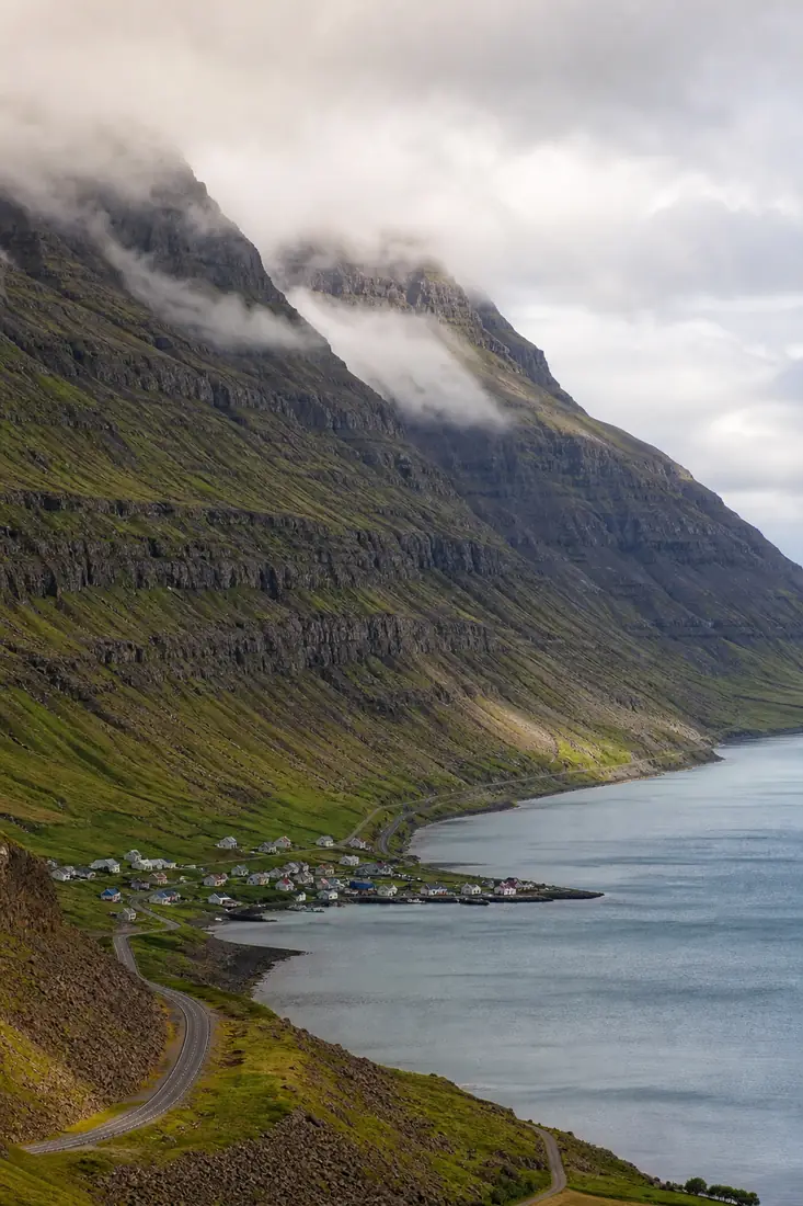 Steile isländische Basaltberge über einem Fjord und kleinem Küstenort