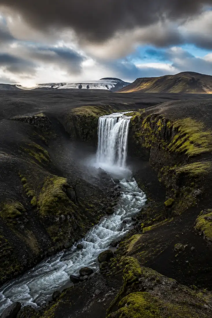 Isländische Vulkanlandschaft mit Wasserfall, schwarzem Gestein und Gletscher