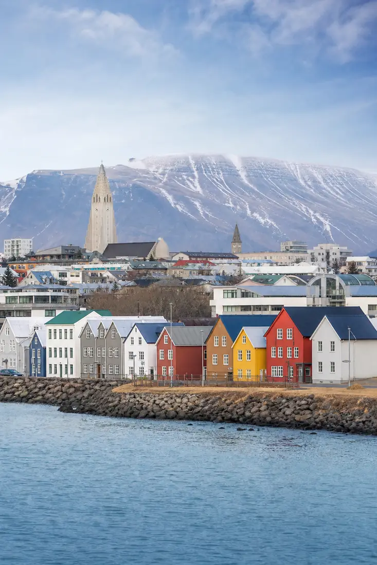 Reykjavíks farbige Häuser und Hallgrímskirkja vor verschneiten Bergen an der Küste